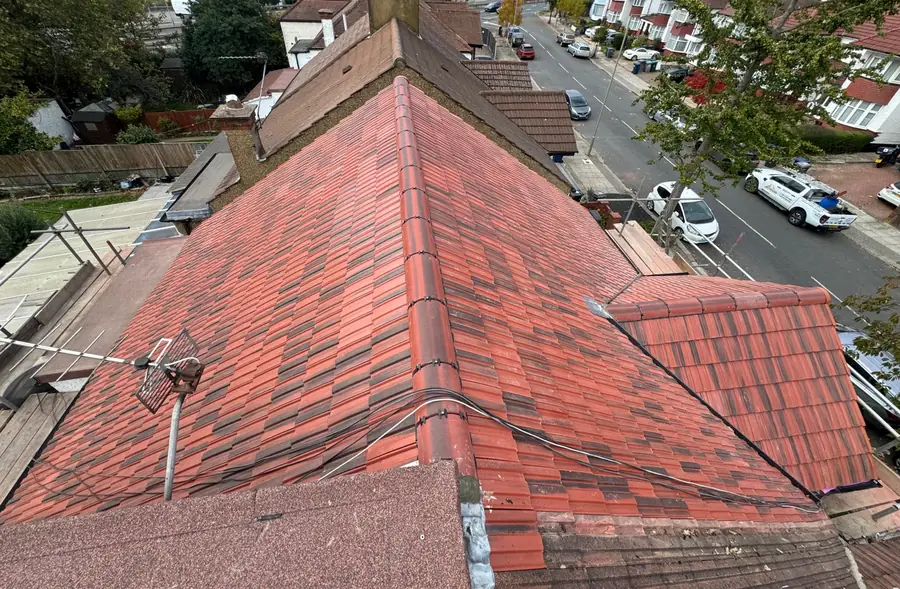 New red tiled hip roof seen from the scaffold, with the street and parked cars below